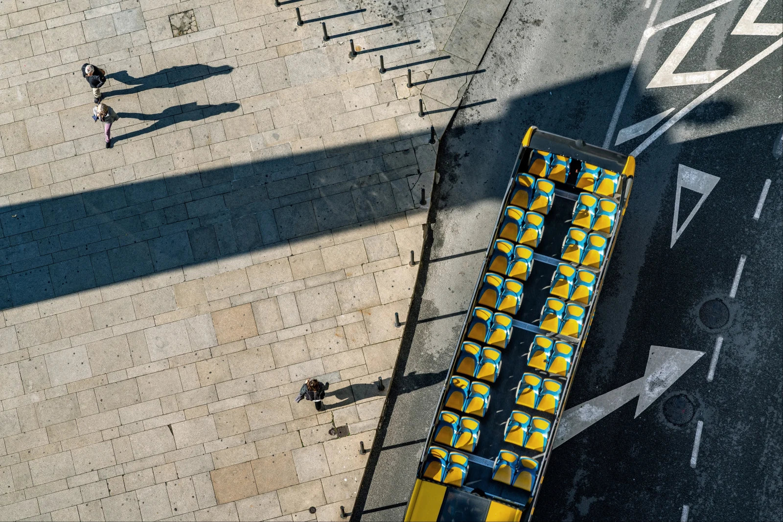 A yellow open-top tour bus seen from above beside strong street geometry in Porto